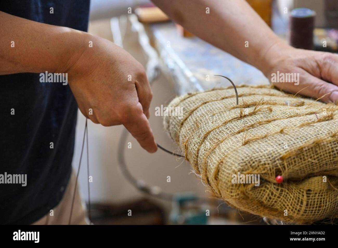 L'artigiano della tappezzeria cuce un pacchetto stampato pieno di cocco (fibra di cocco) con un ago curvo per creare un arredamento moderno o antico, storico Foto Stock