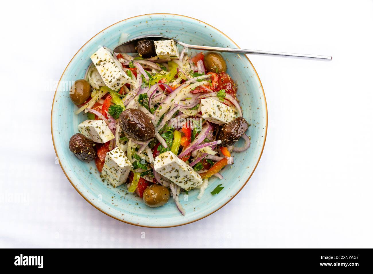 Insalata greca con cipolle, peperoni, olive, feta ed erbe aromatiche in una ciotola, piatto vegetariano mediterraneo su un tavolo bianco, spazio per copiare, vista dall'alto Foto Stock