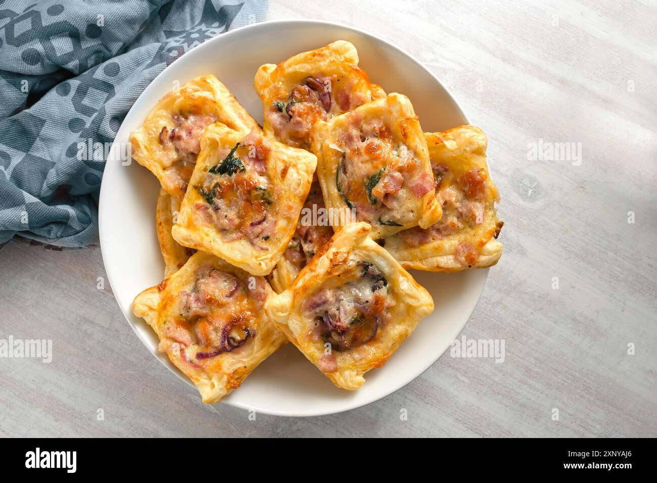 Quadrati di pasta sfoglia al forno con prosciutto, cipolla, erbe aromatiche e formaggio in una ciotola, snack finger food per una festa calda o fredda a buffet, vista dall'alto Foto Stock