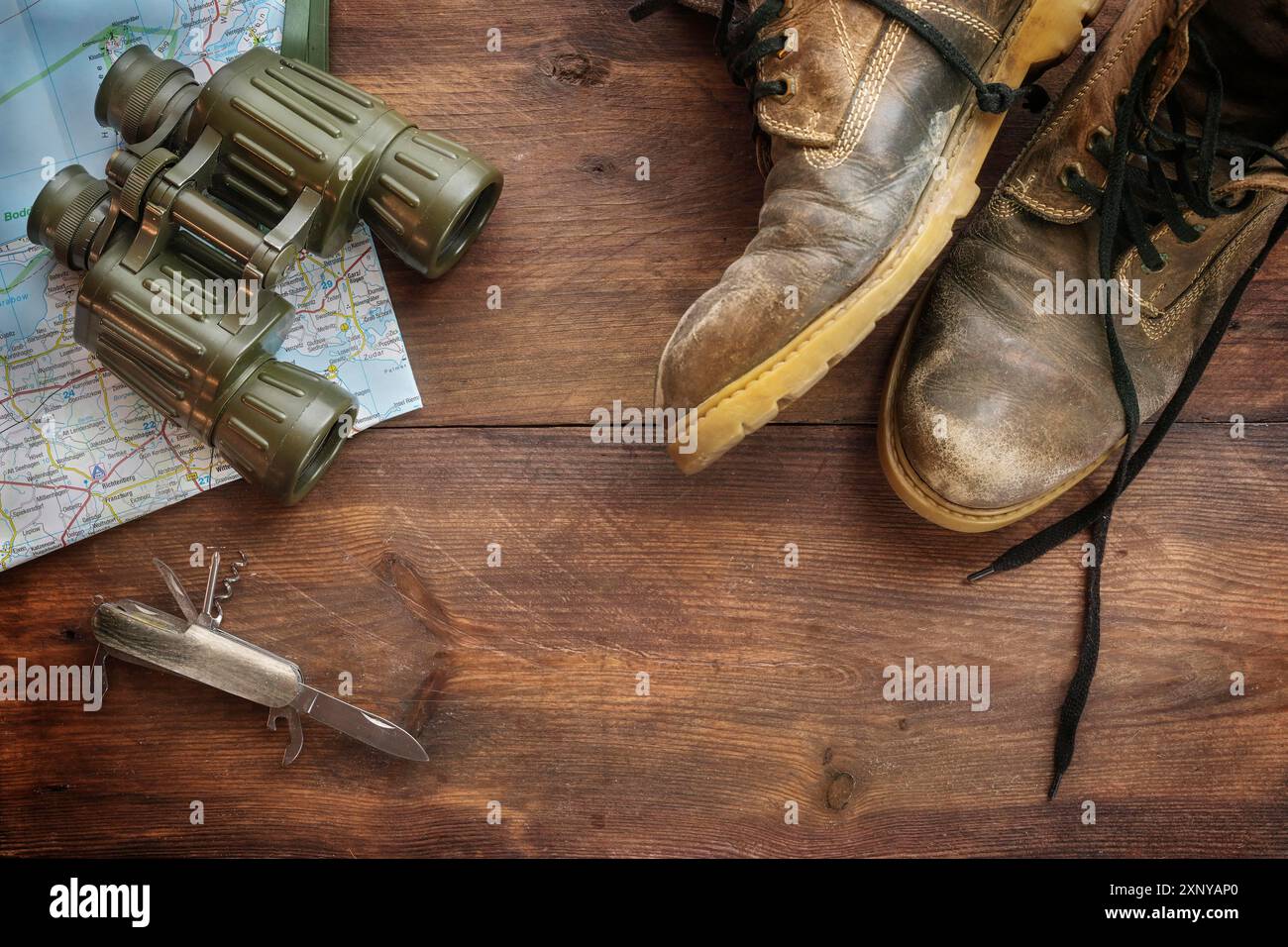 Vecchi stivali da trekking in pelle, binocoli, mappa e un coltello tascabile su legno rustico scuro, concetto per viaggi, escursioni e vacanze avventurose, angolo alto Foto Stock