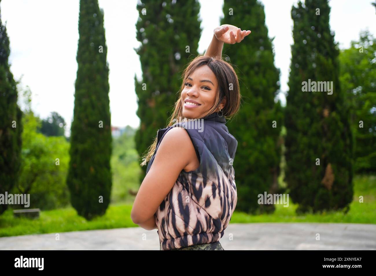 Potente ballerina latina sorridente che solleva il braccio danzando salsa in un parco Foto Stock