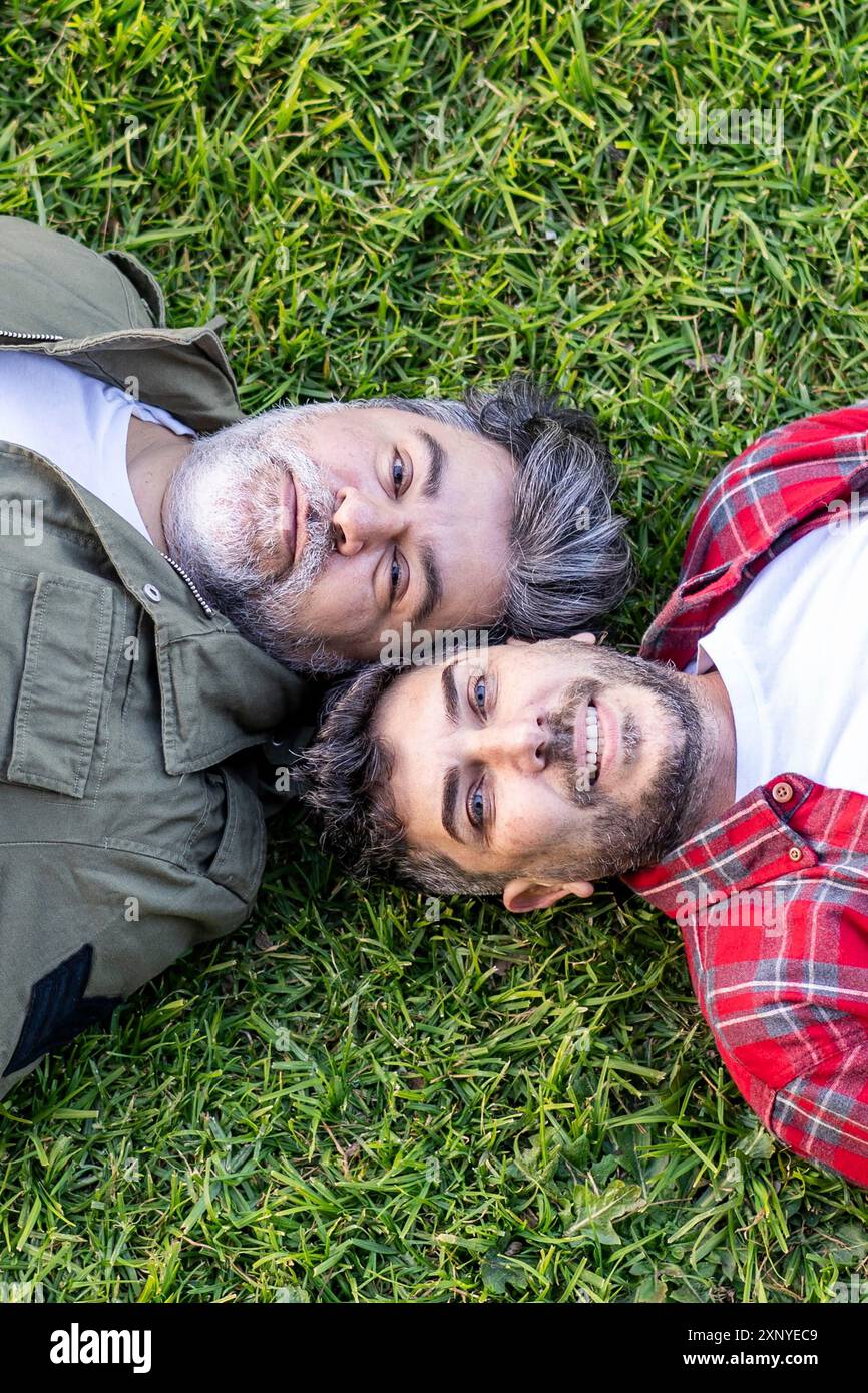 Vista dall'alto di una coppia gay ispanica sdraiata sull'erba mentre guarda la telecamera. Scatto verticale Foto Stock