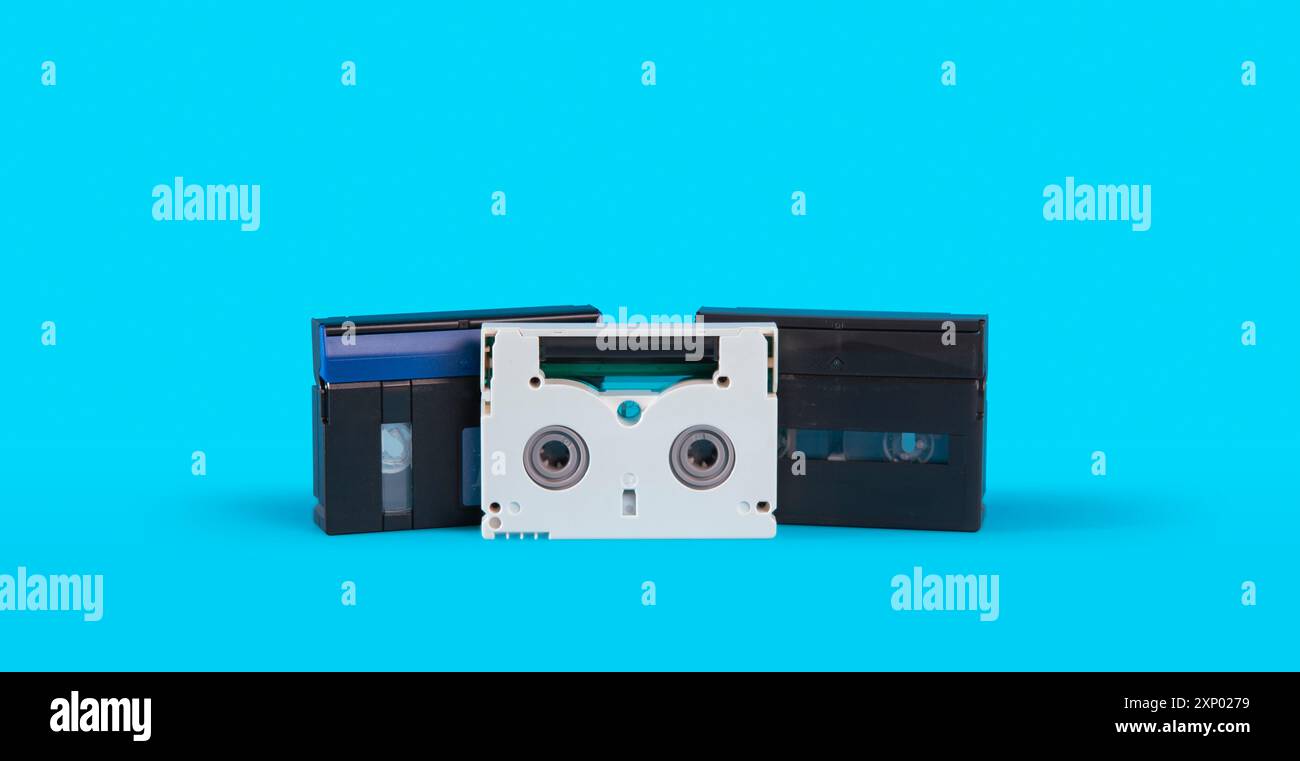 Vista frontale di tre vecchie cassette mini DV in bianco e nero su una superficie blu su sfondo blu Foto Stock