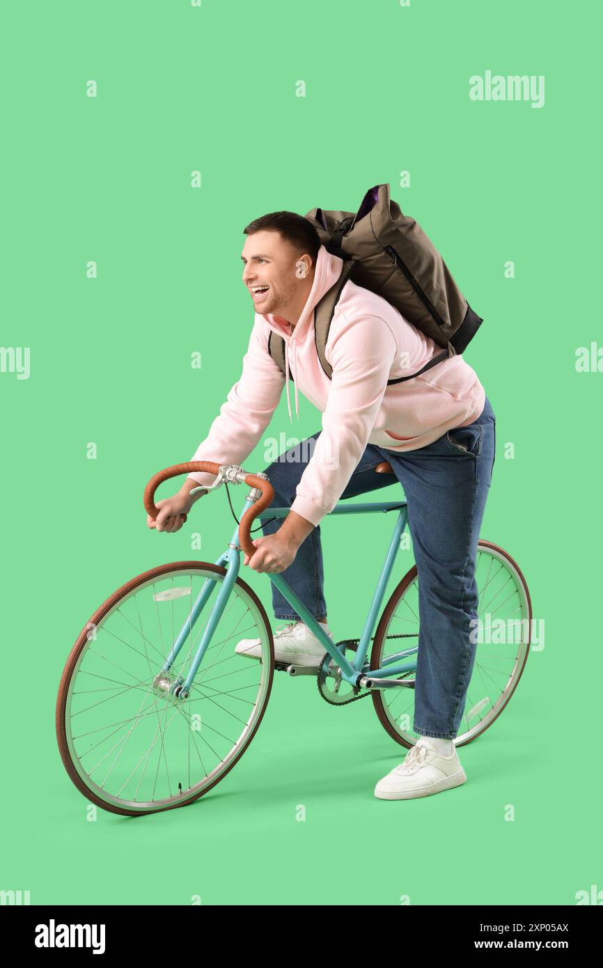 Turista maschile con zaino in bicicletta su sfondo verde Foto Stock