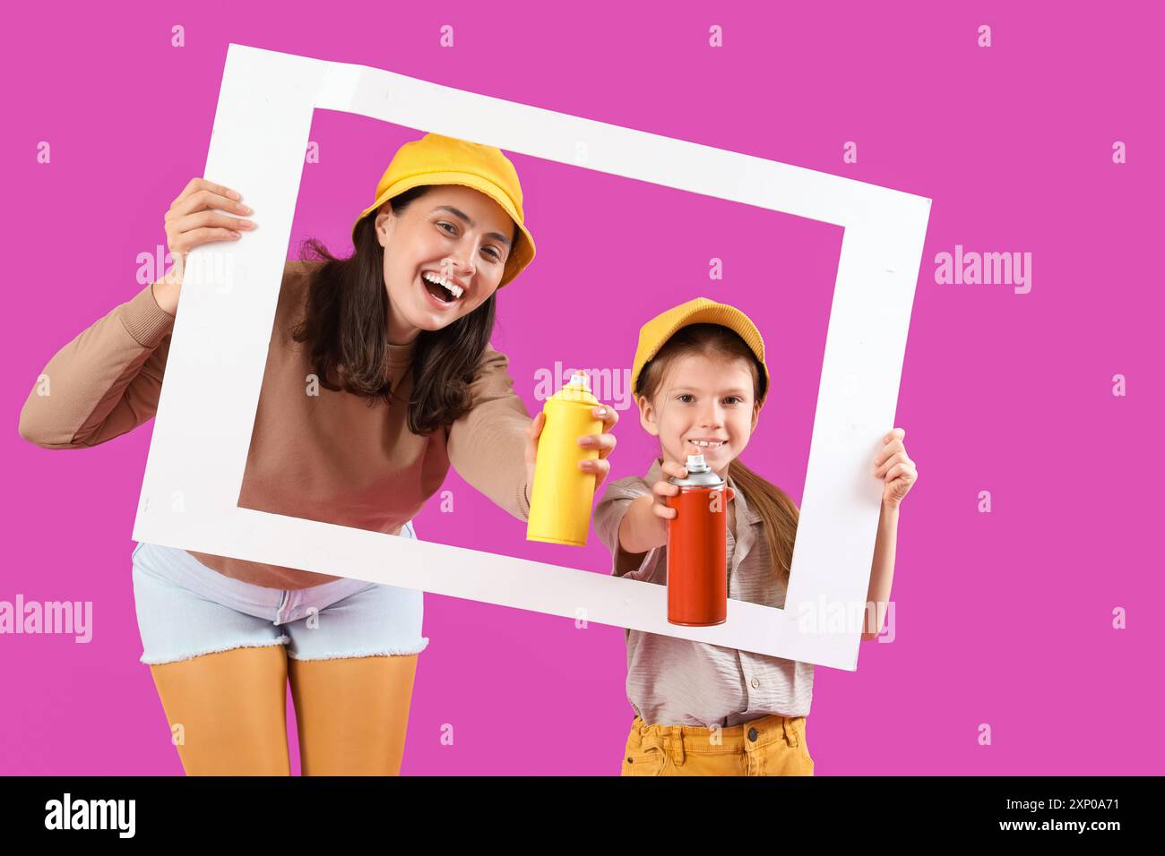 La bambina e sua madre hanno in mano lattine di vernice spray e cornice di carta su sfondo viola Foto Stock