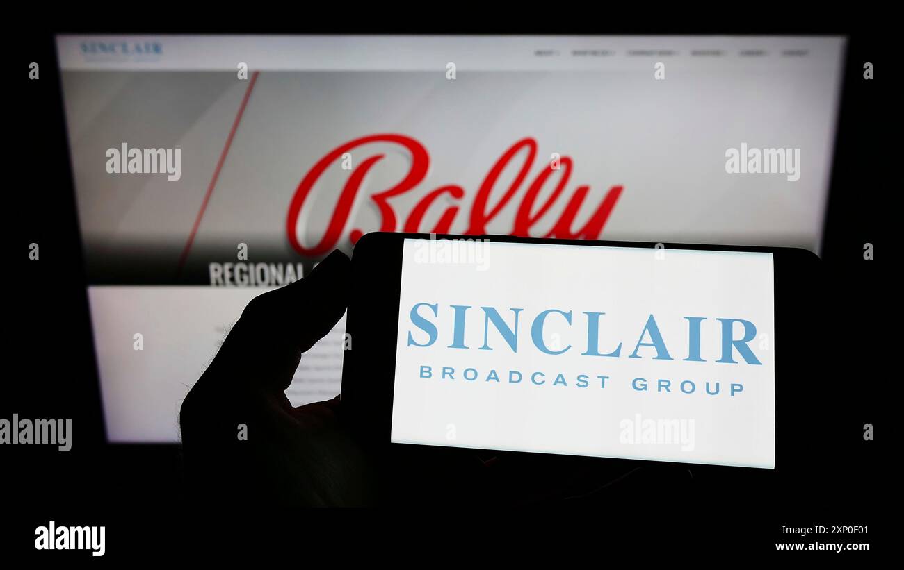 Stoccarda, Germania, 03-30-2022: Persona che detiene il cellulare con il logo della società americana Sinclair Broadcast Group Inc. (SBG) sullo schermo di fronte Foto Stock