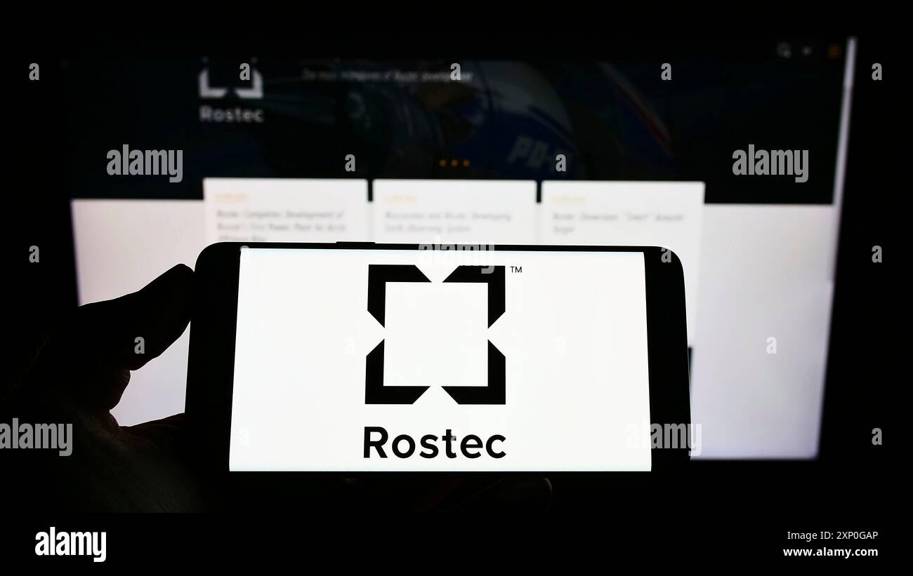 Stoccarda, Germania, 05-08-2022: Persona che detiene il cellulare con il logo della società di difesa russa Rostec sullo schermo di fronte alla pagina web aziendale. Concentrati su Foto Stock