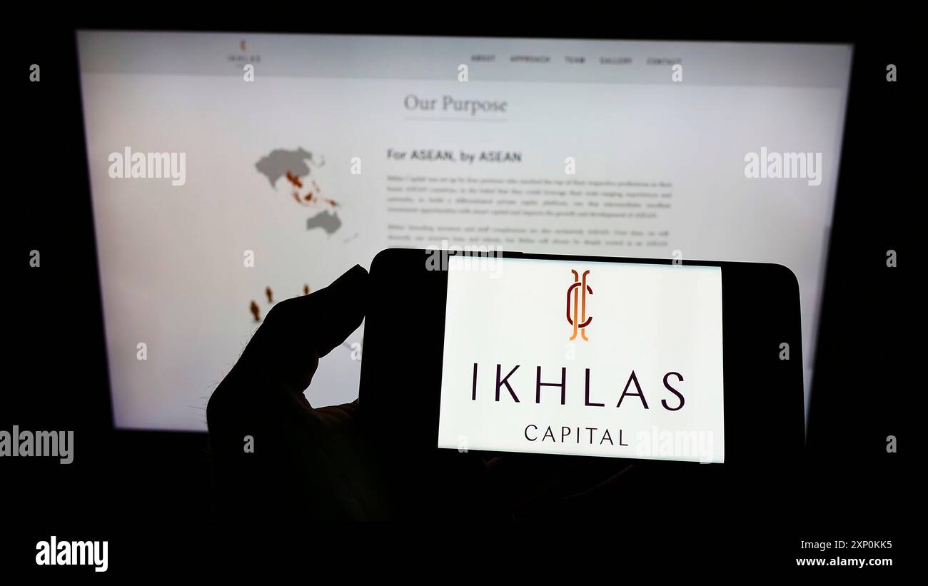 Stoccarda, Germania, 01-16-2022: Persona che detiene il cellulare con il logo della società Ikhlas Capital Singapore Pte. Ltd. Sullo schermo davanti all'azienda Foto Stock