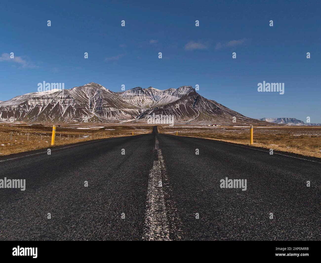 Splendida vista della strada dritta e vuota (percorso 54) con una prospettiva in diminuzione sulla penisola di Snaefellsnes, Islanda occidentale, con aspre montagne innevate Foto Stock