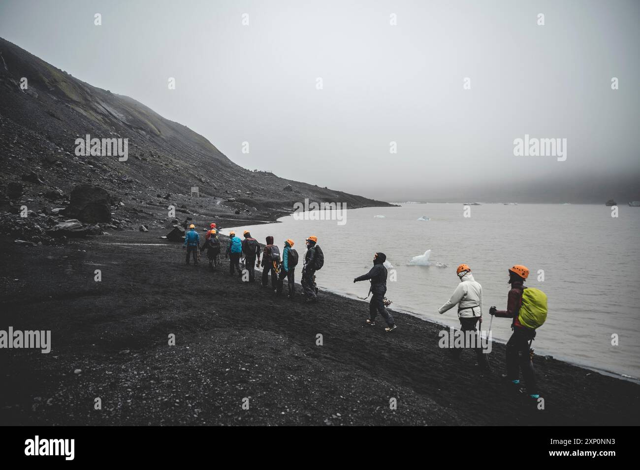 Gruppo di escursionisti con casco protettivo che si allontana dal ghiacciaio Solheimajokull durante le piogge, in Islanda Foto Stock