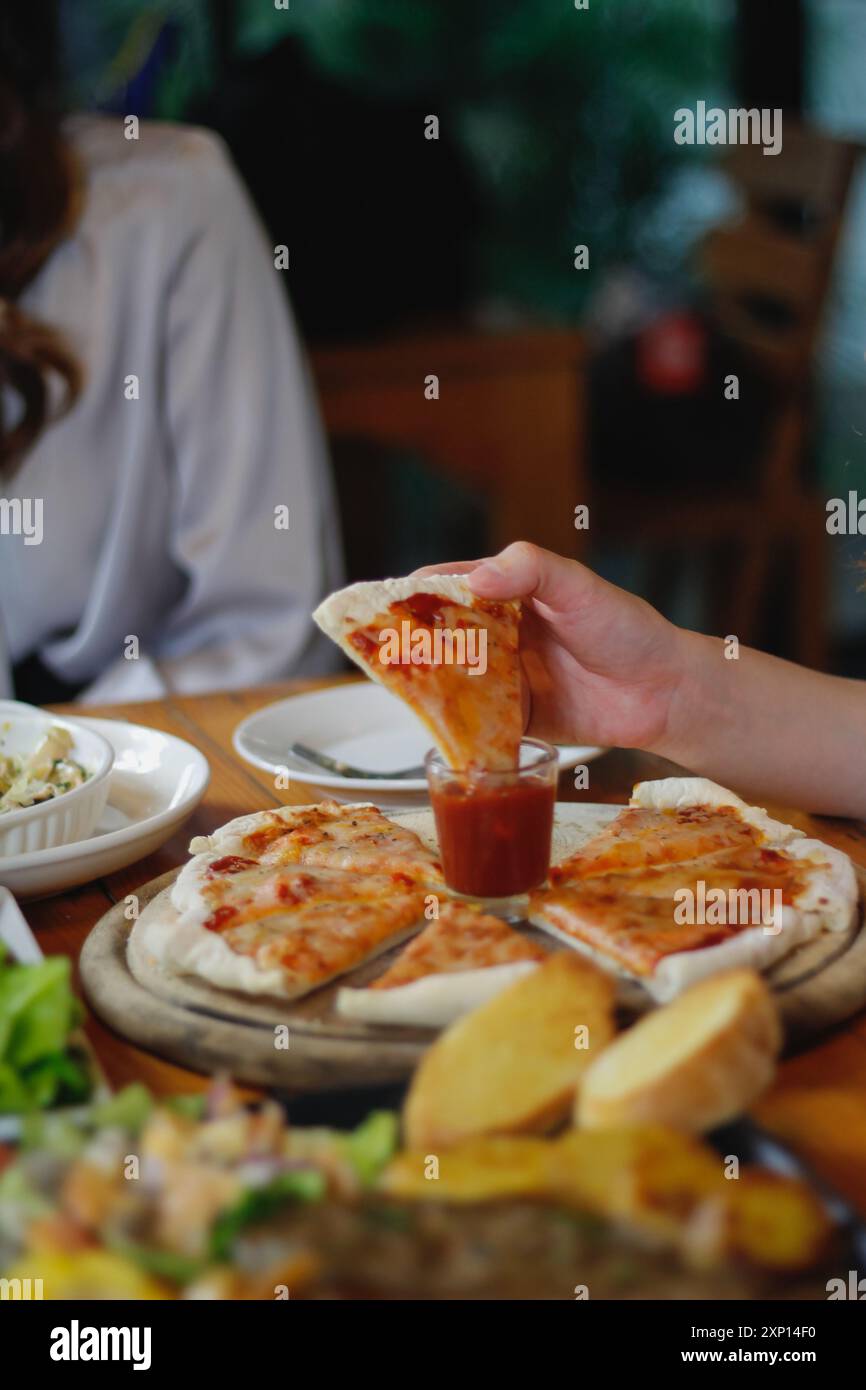 Una giovane donna è felice di vedere il cibo sul tavolo e scegliere il menu della pizza da mangiare con buon gusto. I menu di pizza sono perfetti per banchetti tra frien Foto Stock Una giovane donna è felice di vedere il cibo sul tavolo e scegliere il menu della pizza da mangiare con buon gusto. I menu di pizza sono perfetti per banchetti tra frien Foto Stock