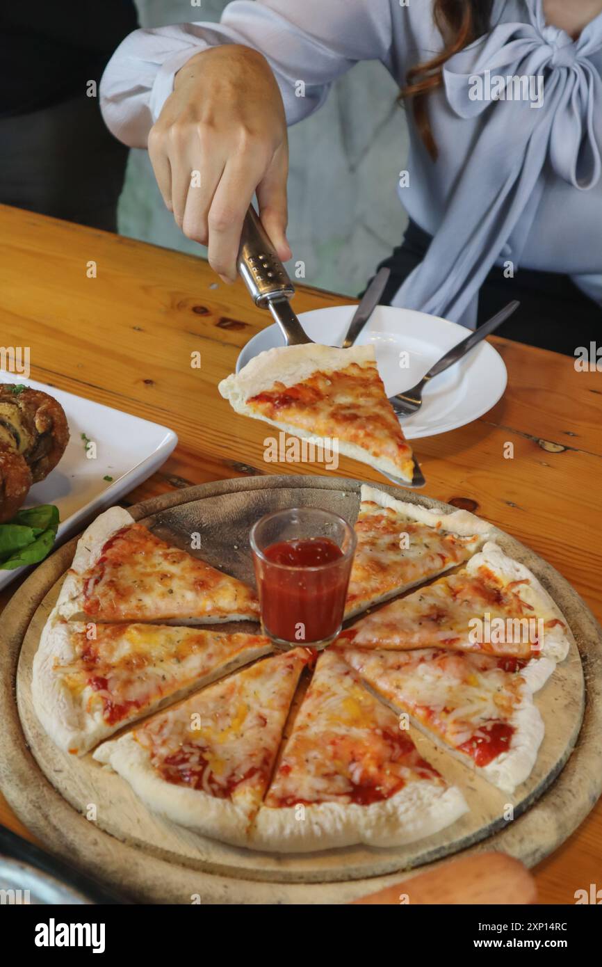 Una giovane donna è felice di vedere il cibo sul tavolo e scegliere il menu della pizza da mangiare con buon gusto. I menu di pizza sono perfetti per banchetti tra frien Foto Stock Una giovane donna è felice di vedere il cibo sul tavolo e scegliere il menu della pizza da mangiare con buon gusto. I menu di pizza sono perfetti per banchetti tra frien Foto Stock