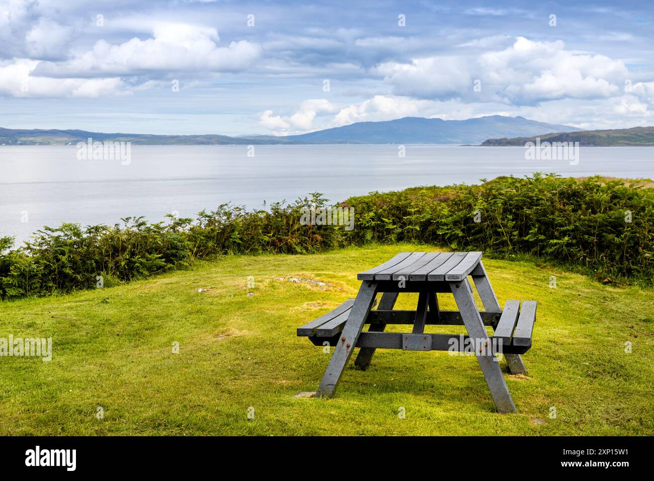 Tavolino da picnic rettangolare in materiale composito in stile panchina in campagna, circondato dall'erba con vista sul mare sullo sfondo Foto Stock