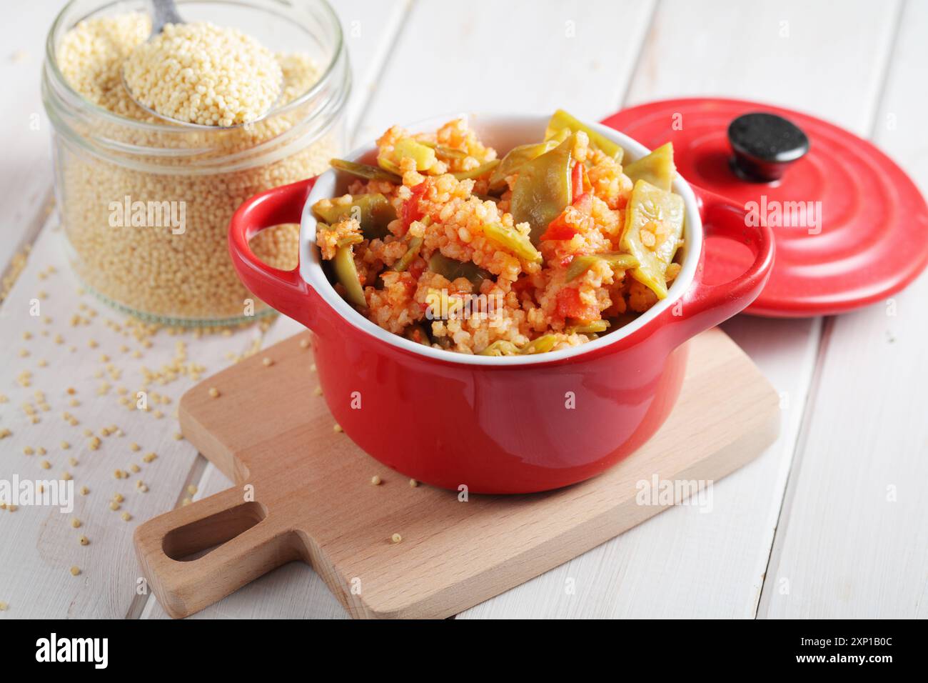 Porridge di miglio con fagioli verdi e pomodoro in pentola rossa su un tavolo rustico Foto Stock