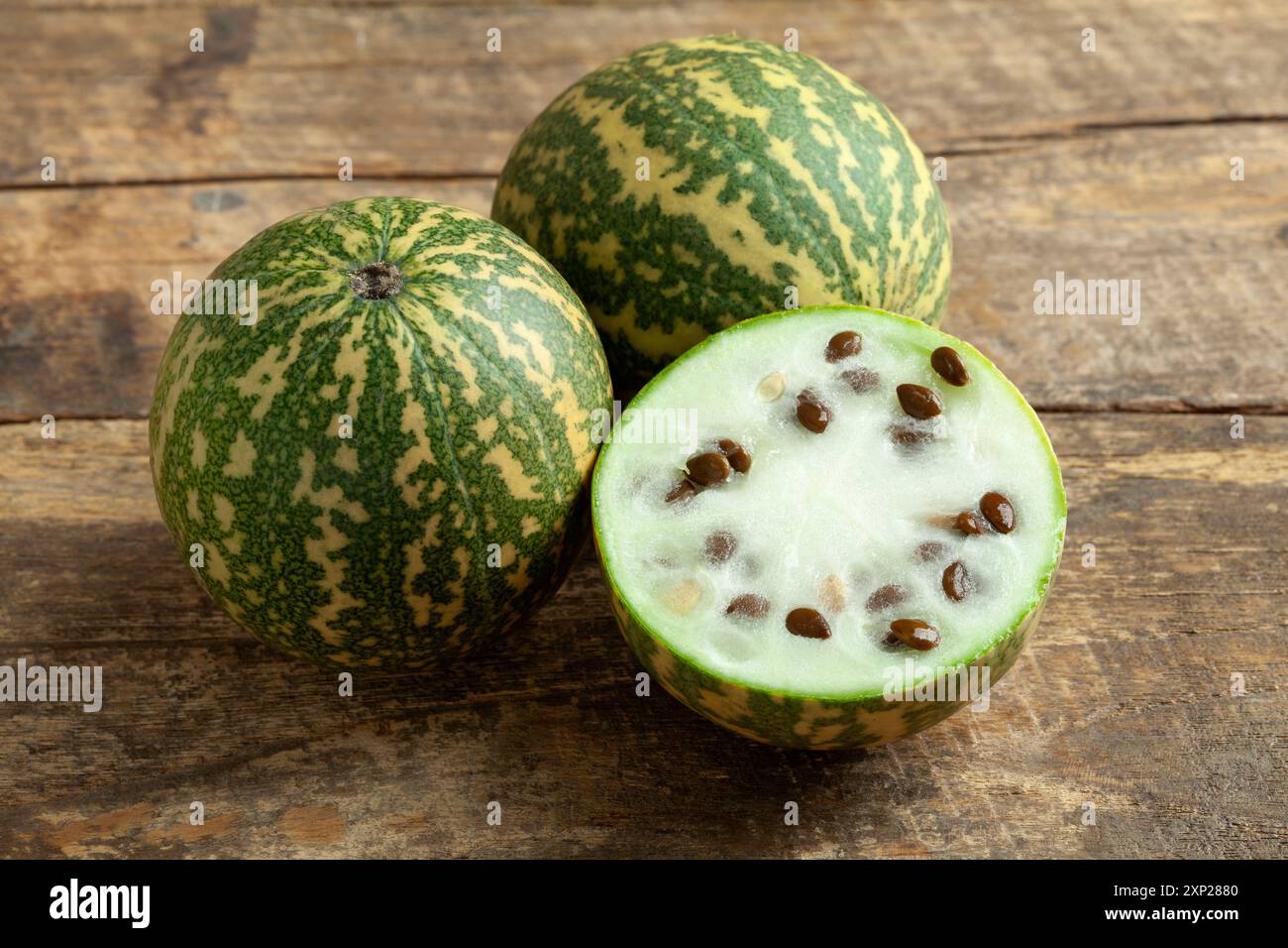 Piccolo melone di citrona rosso intero e tagliato a metà su fondo di legno da vicino Foto Stock