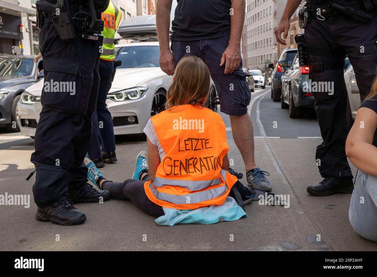 Augusta, Baviera, Germania - 3 agosto 2024: Gli attivisti dell'ultima generazione bloccano una strada nel centro di Augusta e arrestano il traffico. La polizia cerca di fermare gli attivisti prima di bloccare la strada *** Aktivisten der letzten Generation blockieren eine Straße in der Innenstadt von Augsburg und legen den Verkehr lahm. Die Polizei versucht die Aktivisten aufzuhalten bevor Sie die Straße blockieren Foto Stock