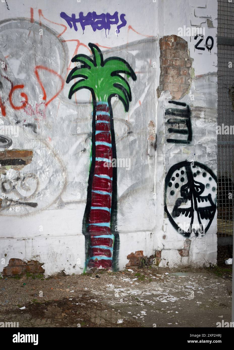 Graffiti raffiguranti una palma vibrante e motivi astratti su un muro urbano in difficoltà, a simboleggiare lo scontro tra la natura e la vita cittadina. Foto Stock