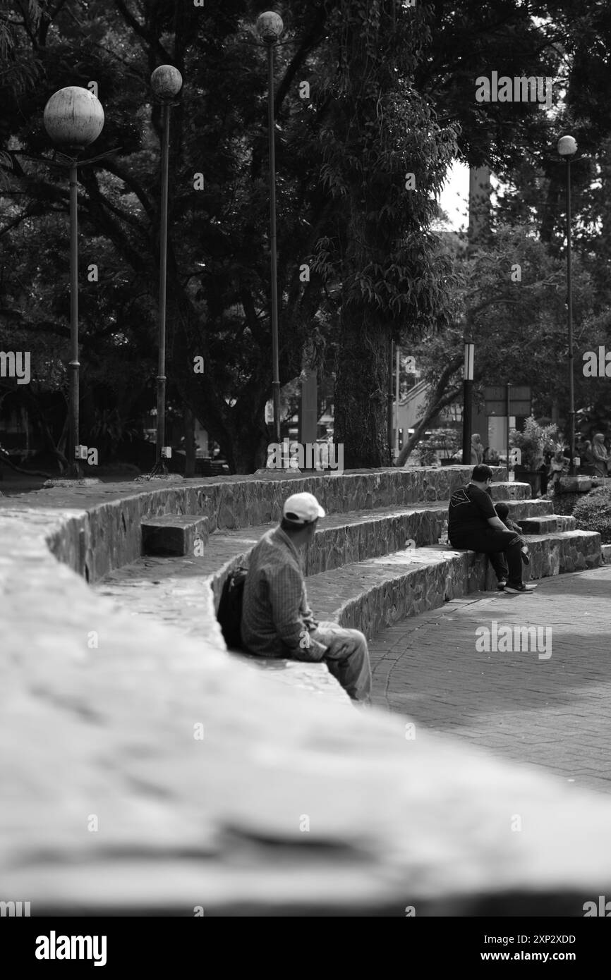 Un vecchio seduto su una panchina terrazzata nel mezzo della città durante il giorno Foto Stock