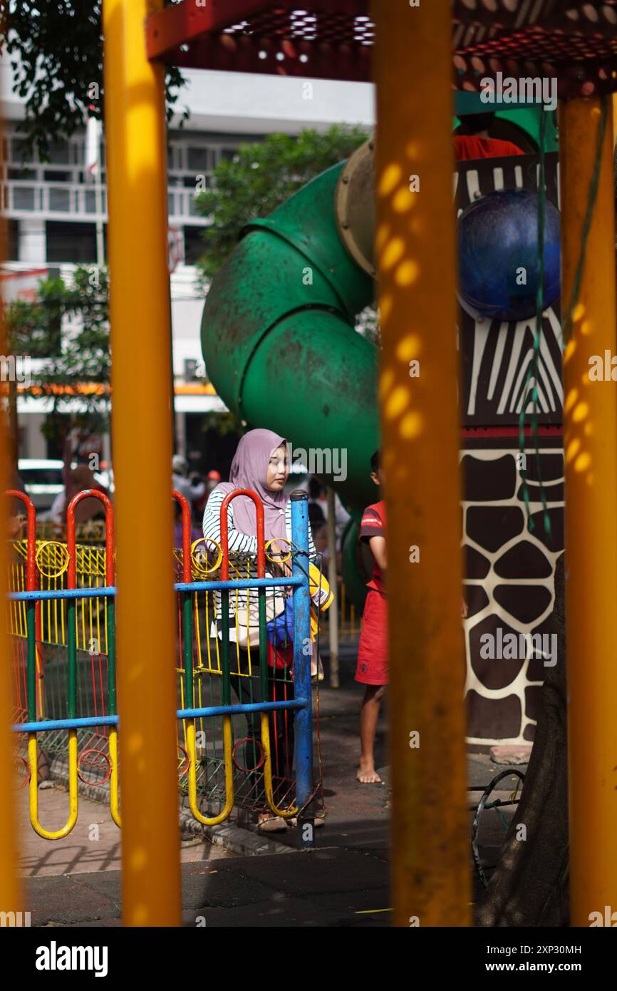 Una madre che aspetta il suo bambino che gioca in un parco giochi all'aperto la mattina in uno spazio pubblico aperto Foto Stock