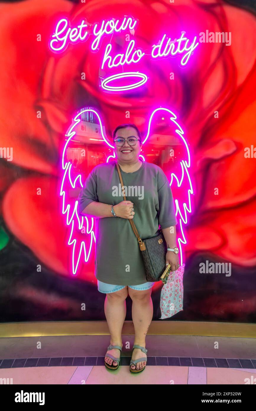 Una signora posa per una fotografia davanti a un paio di ali d'angelo rosa al neon. Foto Stock