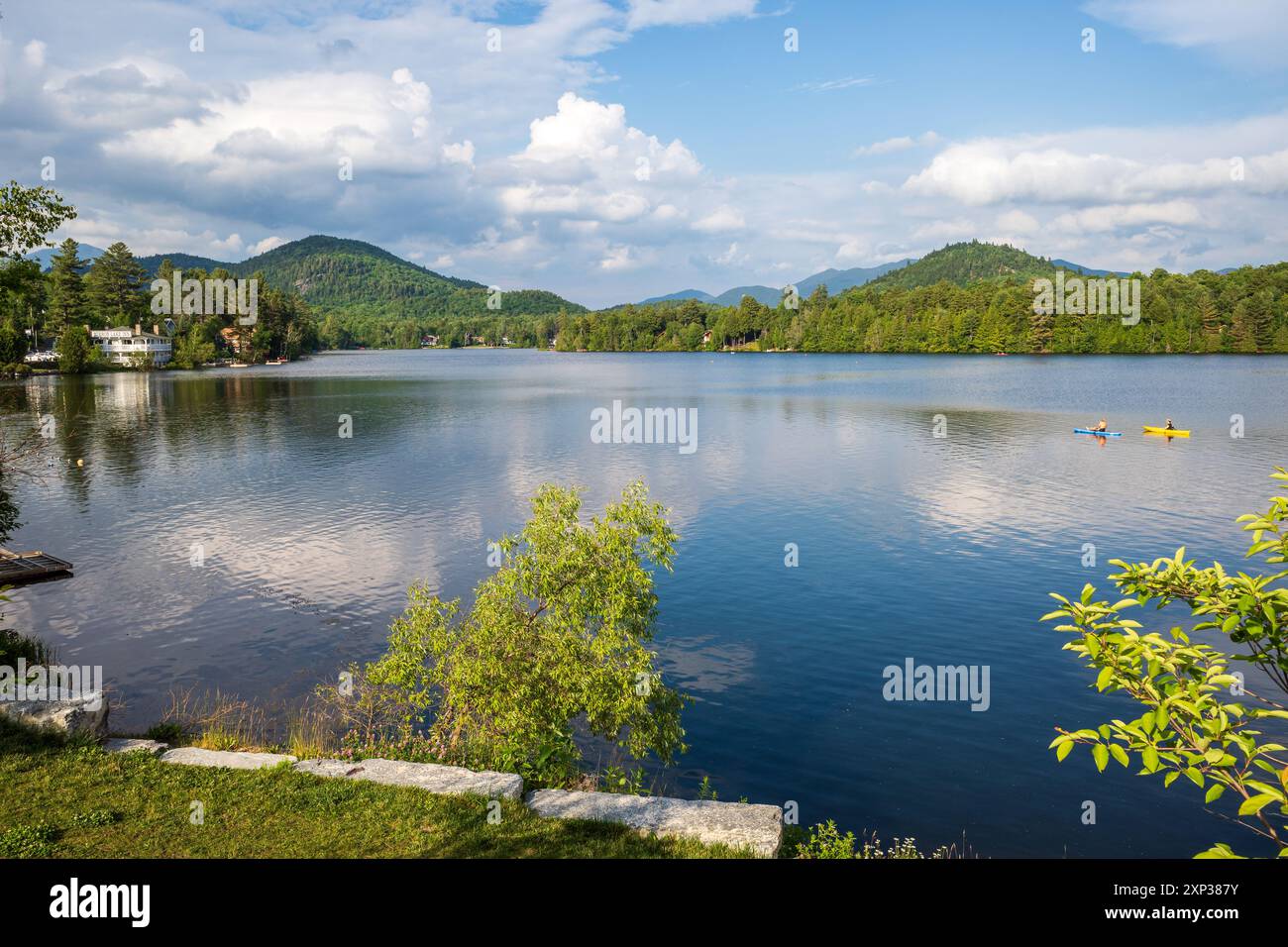 Il tranquillo lago Mirror di Lake Placid, nella parte settentrionale dello stato di New York, offre canoe blu e gialle sulle acque calme, con un cielo blu mozzafiato e maestoso Foto Stock