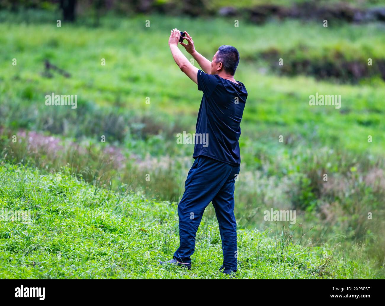Un turista maschio in piedi in campo aperto per scattare una foto con il suo cellulare. Sichuan, Cina. Foto Stock