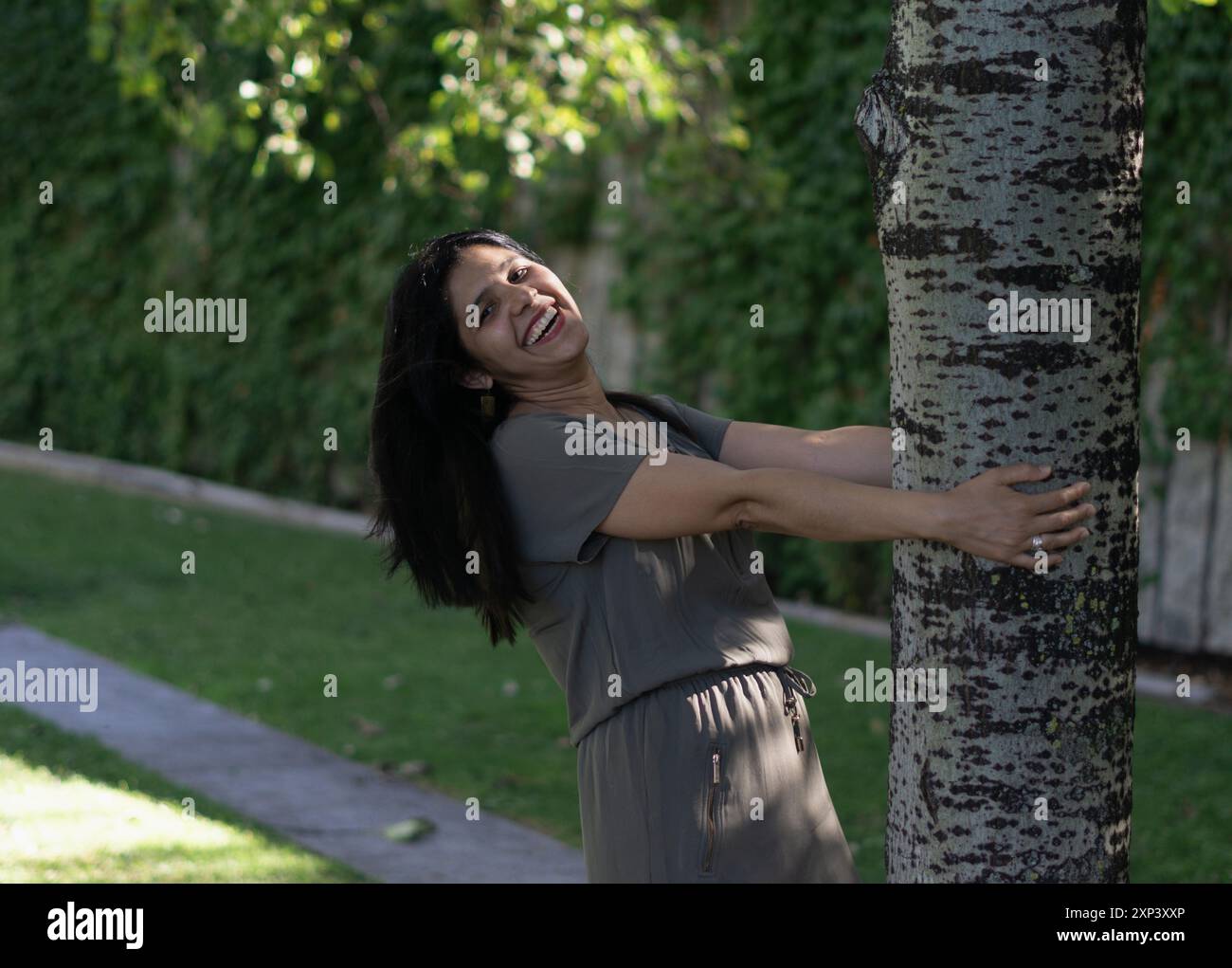 Una donna sta abbracciando un albero in un parco. Lei sorride ed è felice. Concetto di gioia e connessione con la natura Foto Stock