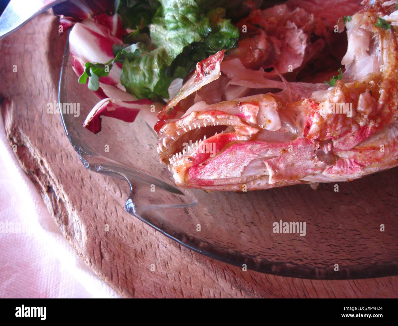 Testa di pesce alla griglia condita su un piatto di legno con insalata laterale Foto Stock