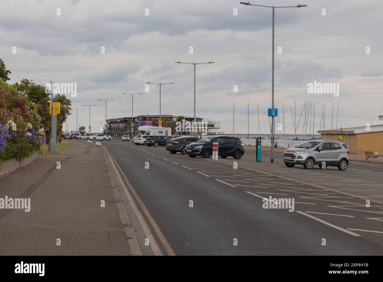 Southend on Sea, Regno Unito. 3 agosto 2024. Una giornata nuvolosa lungo una strada costiera costeggiata da auto parcheggiate e alti semafori. I pedoni camminano vicino al verde sulla sinistra, mentre i montanti delle barche a vela e un edificio moderno suggeriscono la vicinanza a un porticciolo. Cattura le infrastrutture, i trasporti e il tempo libero in una città costiera britannica. La polizia dell'Essex ha implementato un ordine di dispersione e i poteri della sezione 60 per 48 ore a causa di precedenti violenti disordini lungo il lungomare e High Street. Penelope Barritt/Alamy Live News Foto Stock