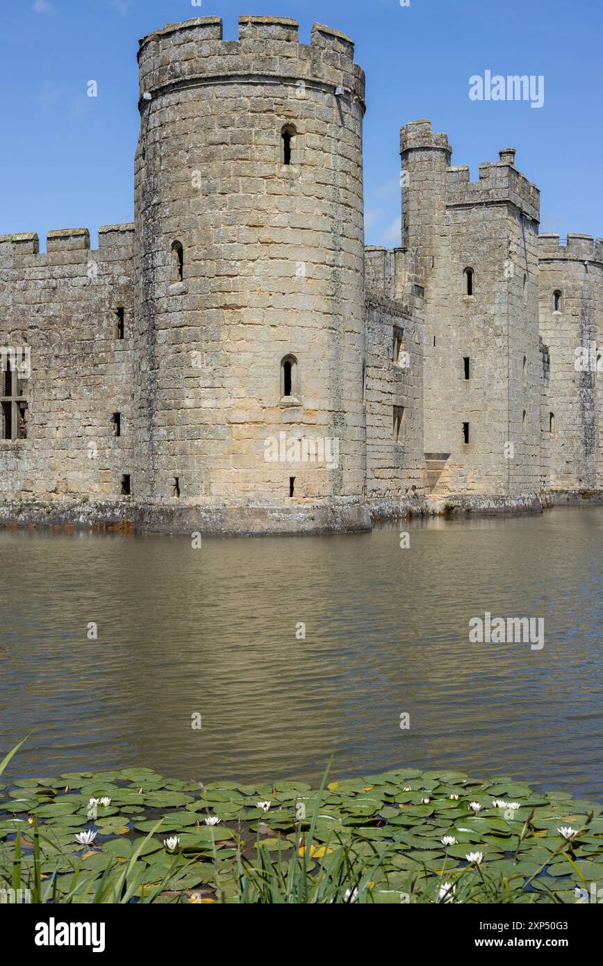 Le imponenti mura medievali del castello di Bodiam nell'East Sussex, Inghilterra, si riflettono nel fossato circostante in un cielo azzurro e soleggiato, giorno d'estate. Foto Stock