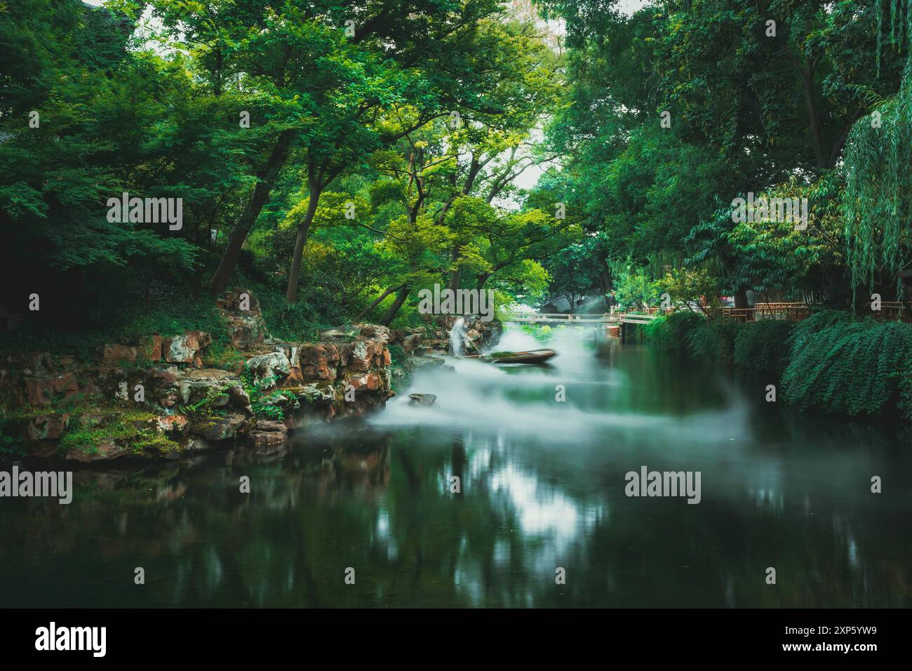 Suzhou, Cina - 11 giugno 2024: Un tranquillo laghetto a Suzhou, in Cina, con un ponte di legno su un'acqua nebbiosa nel giardino dell'umile Amministratore. Foto Stock