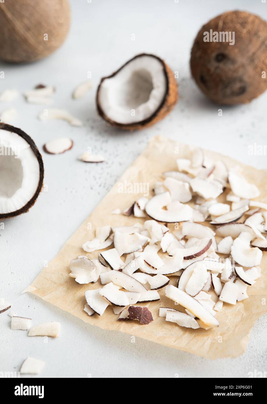 Il cocco organico essiccato affetta le patatine su carta da forno con noce di cocco maturo su sfondo chiaro. Foto Stock