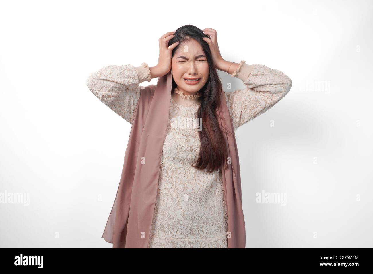 Una donna musulmana asiatica che alza entrambe le mani per tenere la testa si sente stressata e sopraffatta, piange e urla disperatamente, isolata, backgroun bianco Foto Stock