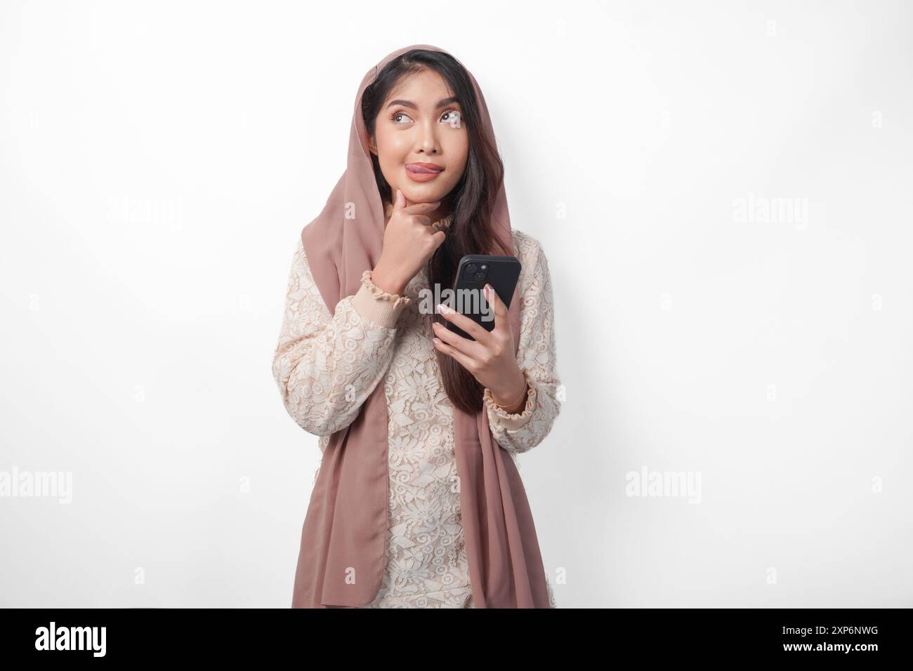 Donna musulmana asiatica affamata in velo hijab pensando a cosa mangiare dopo il digiuno mentre utilizza uno smartphone per ordinare cibi. Concetto Ramadan Foto Stock