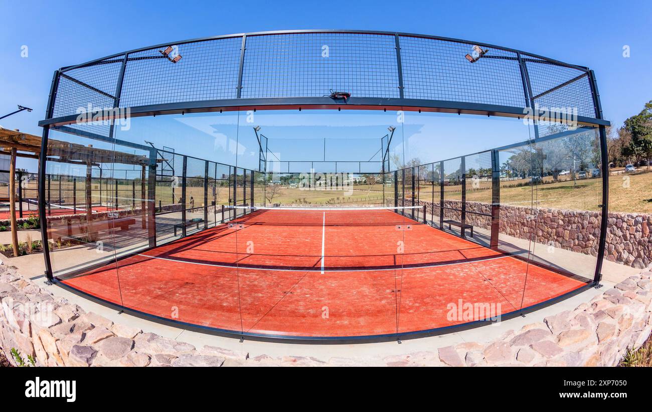 Padel Tennis su superficie rossa astro con campo recintato in vetro in campagna in una giornata di cielo blu. Foto Stock