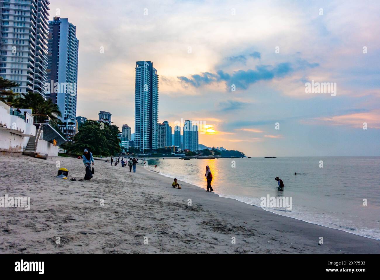 Una vista lungo la spiaggia di Tanjing Tokong a Penang, Malesia al tramonto con il sole che si riflette arancione nel mare e sullo sfondo un paesaggio urbano. Foto Stock