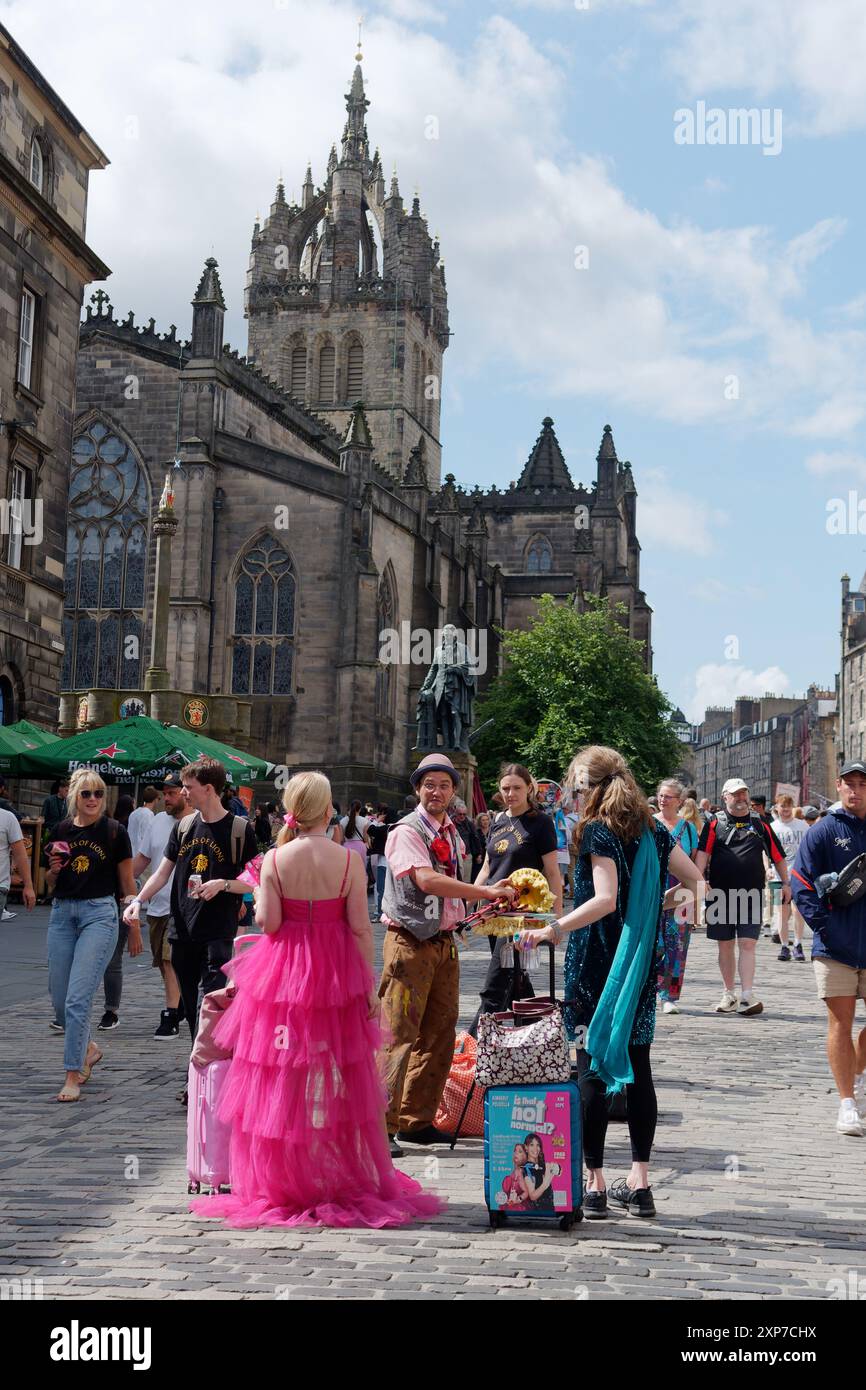 Spettacoli di strada durante l'Edinburgh Fringe Festival. L'uomo mette giù le tubature della borsa mentre parla con una donna con un vestito rosa. 3 agosto 2024 Foto Stock