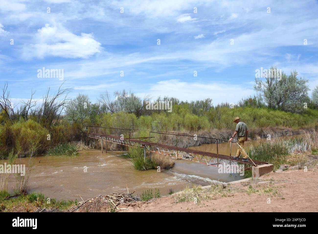 Rusty, metallo, canale di irrigazione, ponte pedonale attraversa il Rio grande, vicino al Sevillita National Wildlife Refuge nel New Mexico. L'uomo sta attraversando. Foto Stock