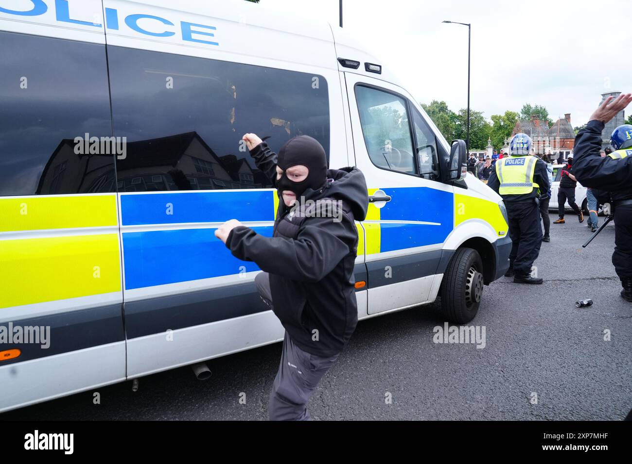 Un uomo mascherato alza la gamba accanto a un furgone della polizia durante una protesta anti-immigrazione a Middlesbrough. Data foto: Domenica 4 agosto 2024. Foto Stock