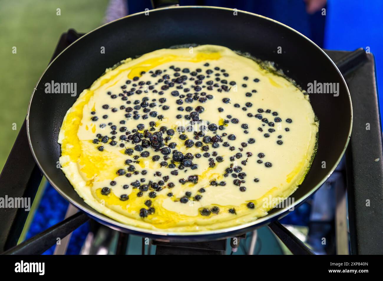 Una pancake ai mirtilli sfrigola nella padella, ricoperta di mirtilli selvatici appena raccolti nel nord della Foresta Nera vicino a Enzklösterle. Il pancake ai mirtilli è una specialità culinaria della Heidelbeerwoche (settimana del mirtillo), tradizionalmente celebrata lì a metà luglio. La tradizione di circa 300 anni della raccolta dei mirtilli selvatici risale alle radure un tempo tagliate per il commercio di fluitazione del legname della regione. Wildbader Straße, Enzklösterle, Baden-Württemberg, Germania. Foto Stock