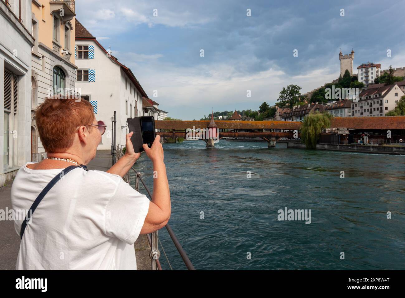 Una donna matura scatta una foto con smartphone del fiume Reuss e dello Spreuer Вridge a Lucerna, in Svizzera Foto Stock