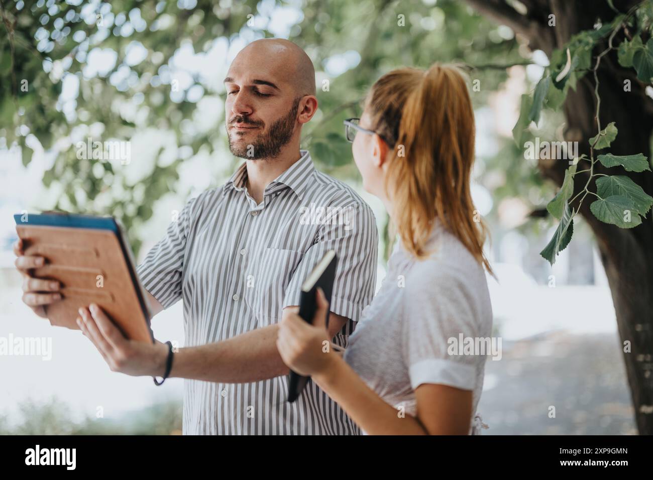 Due colleghi discutono di progetti all'aperto utilizzando tablet e notebook in un parco Foto Stock