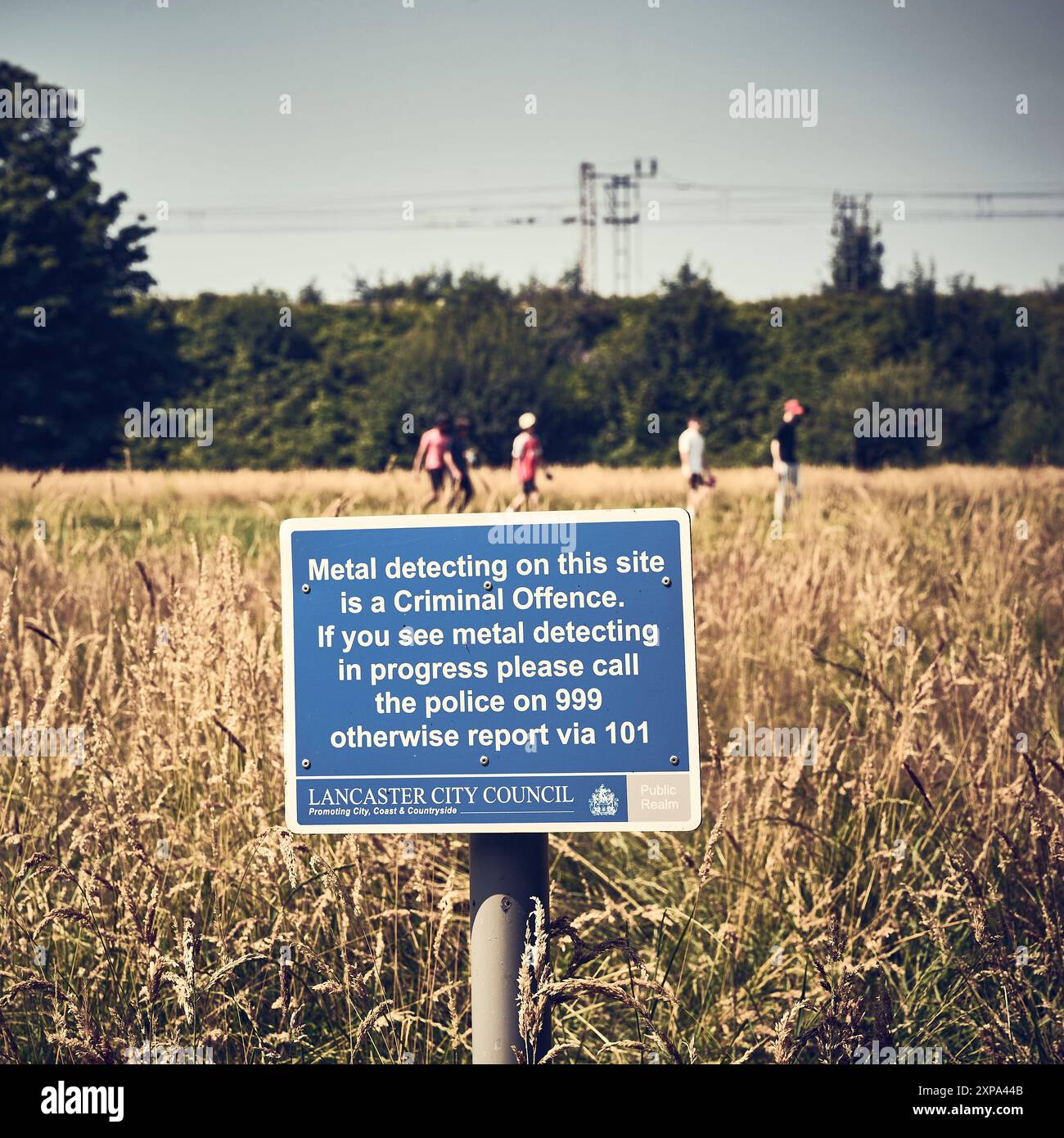 Giovani che camminano dietro un cartello 'no metal Detecting' nel campo di proprietà del consiglio a Lancaster, Regno Unito Foto Stock