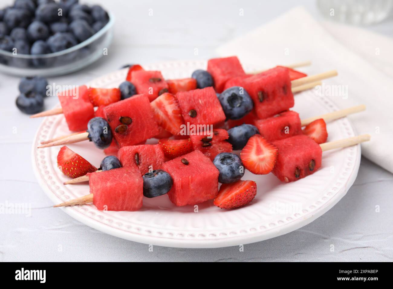 Spiedini con gustosi anguria, fragole e mirtilli su tavola bianca, primo piano Foto Stock