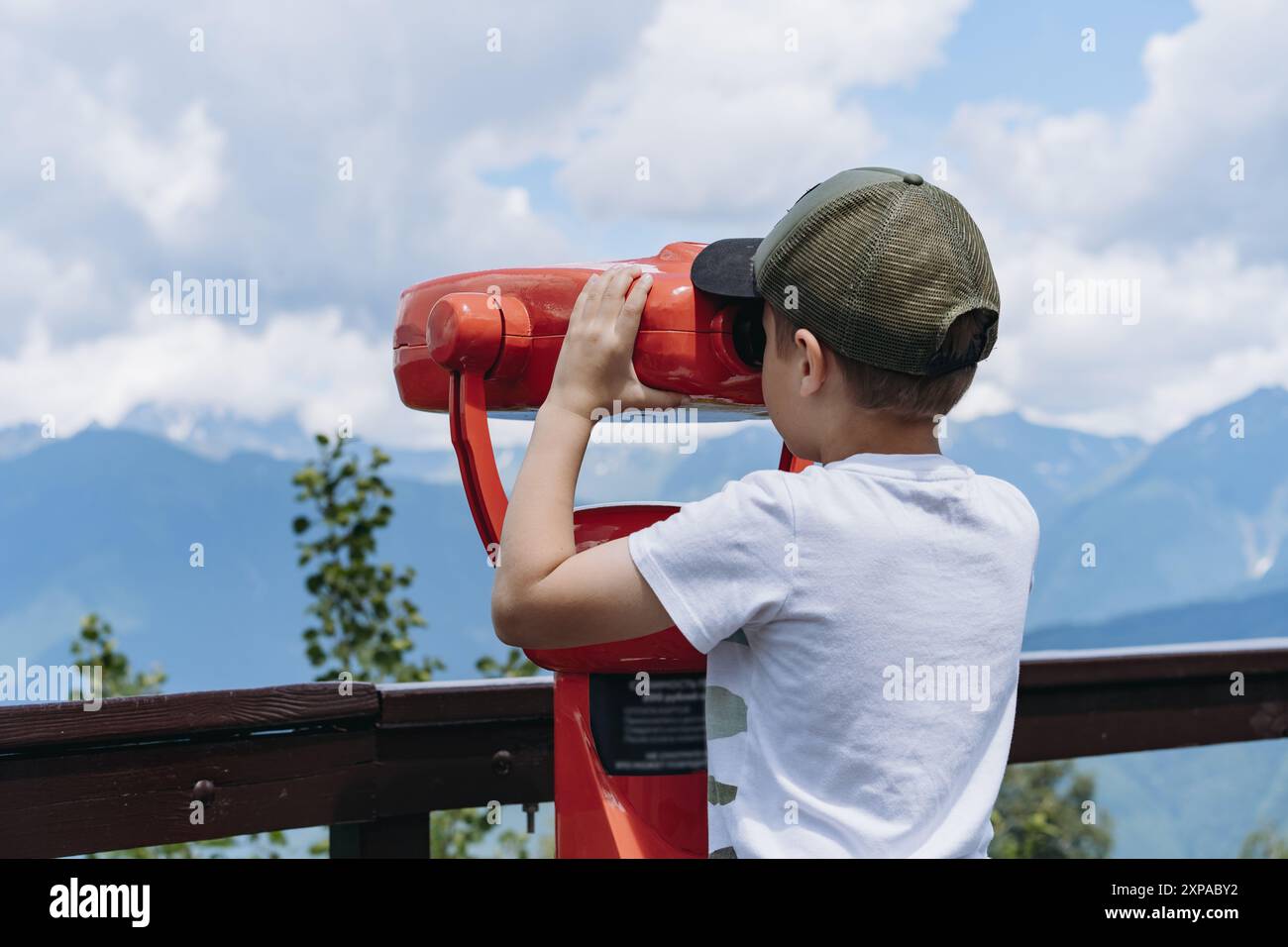 ragazzo che osserva il panorama delle montagne attraverso un binocolo fisso. Foto di alta qualità Foto Stock