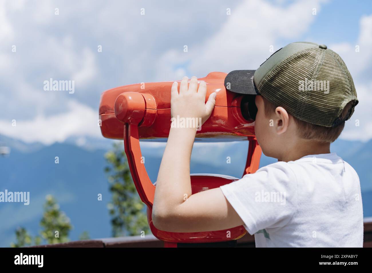 ragazzo che osserva il panorama delle montagne attraverso un binocolo fisso. Foto di alta qualità Foto Stock