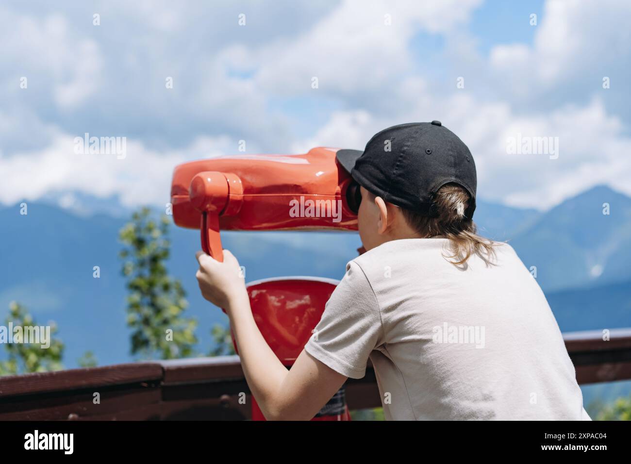 ragazzo che osserva il panorama delle montagne attraverso un binocolo fisso. Foto di alta qualità Foto Stock