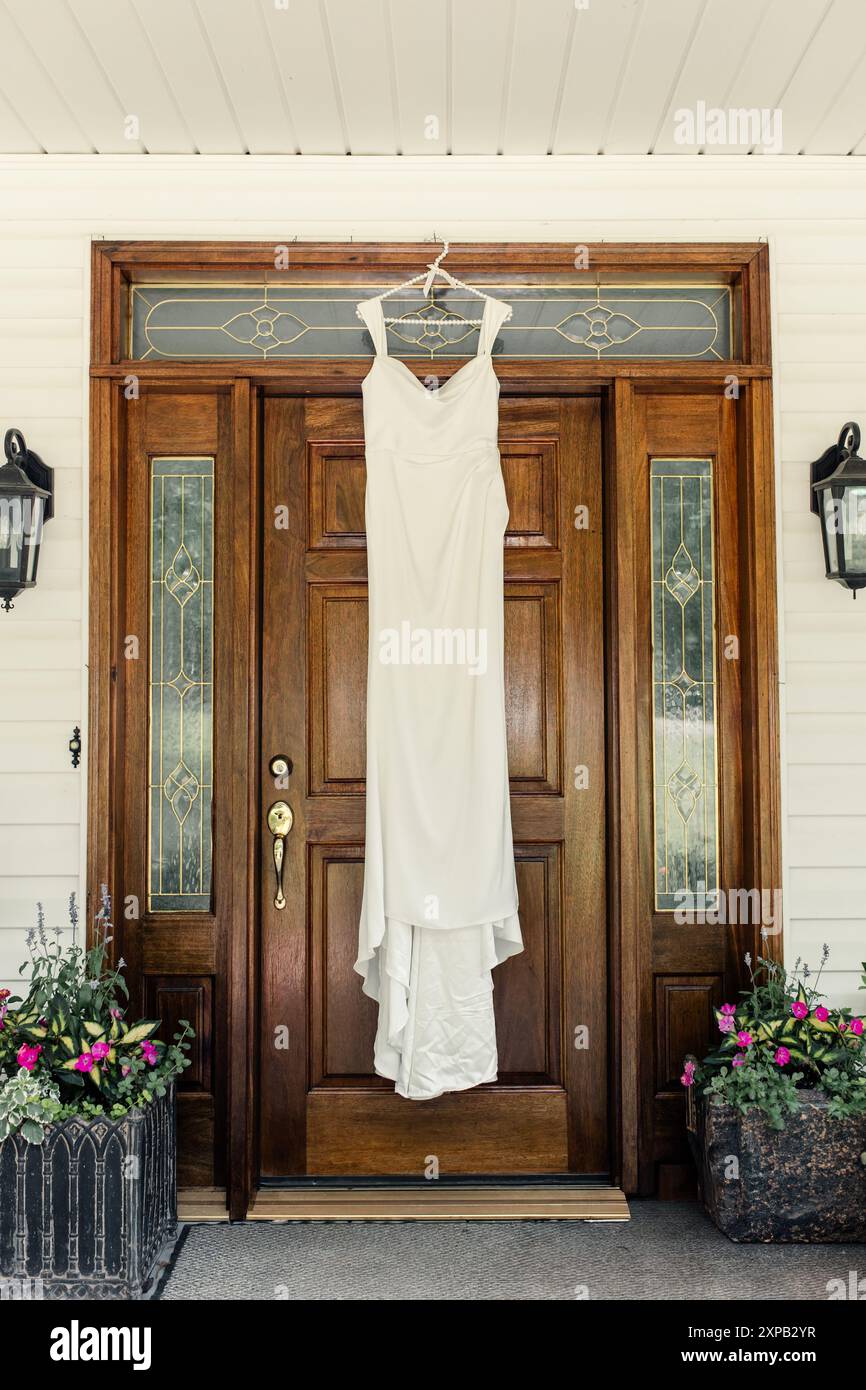 Abito da sposa bianco appeso su una porta d'ingresso in legno. Foto Stock