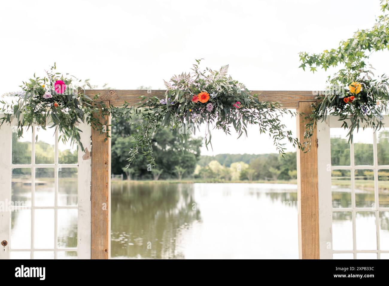 Arco nuziale adornato da fiori e vegetazione vicino a un lago. Foto Stock