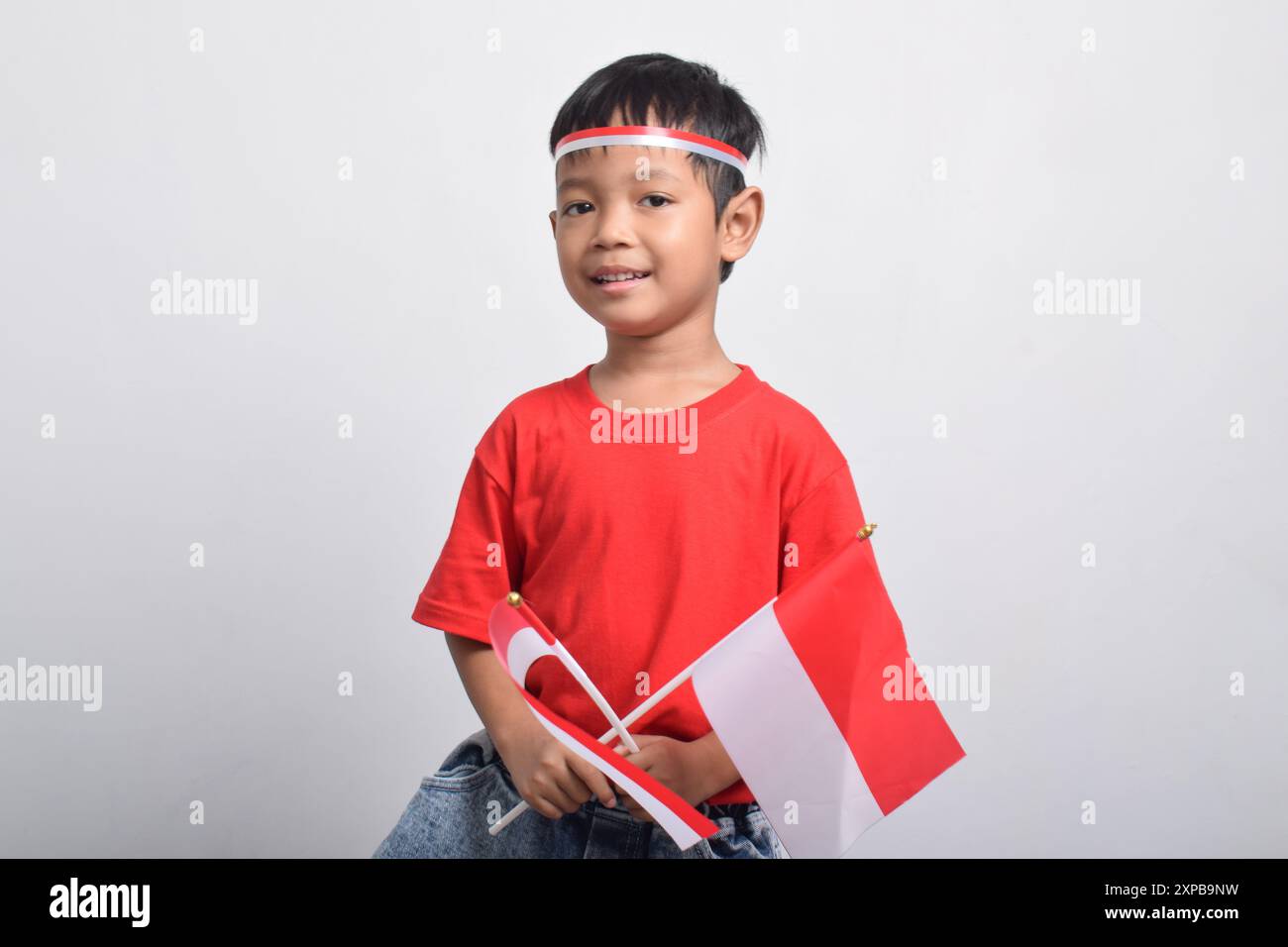 Un ragazzo asiatico felice in camicia rossa con due bandiere e sorridente, isolato su sfondo bianco. Concetto del giorno dell'indipendenza indonesiana. Foto Stock